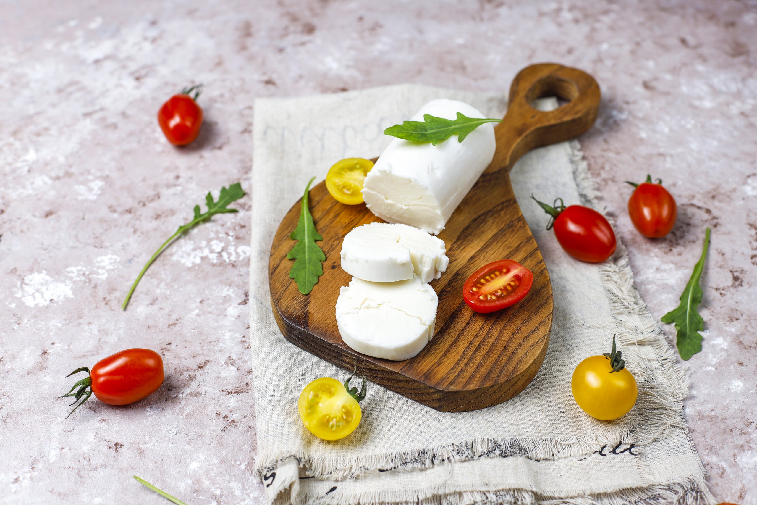 Goat Cheese Slices on Wooden Board with ruccola,cherry tomatoes.